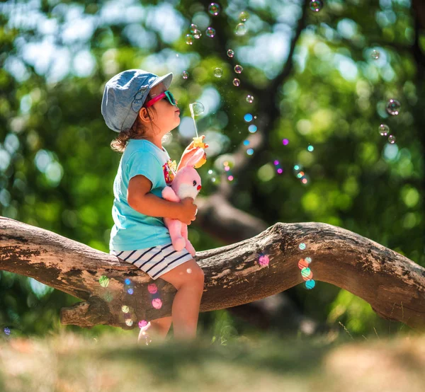 Una niña de un año soplando burbujas de jabón en el parque de verano —  Fotos de Stock