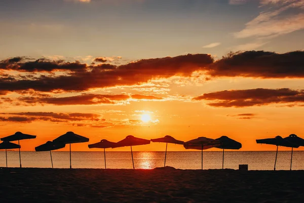 Mar amanecer y silueta de sombrillas de playa — Foto de Stock