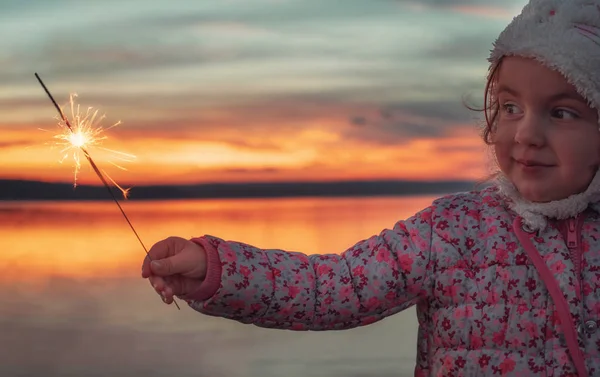 Belle fille avec des étincelles sur le lac au coucher du soleil — Photo
