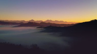 Havadan görünümü sis kapsama gündoğumu, dağlar orman. Uzak dağ silsilesi ve bulutların üstünde vadiler ince tabaka. 