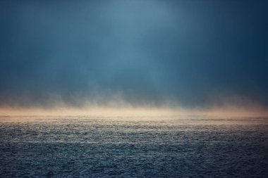 Deniz doğumu ve sisli bir sabah. Mavi dalgalı suyun üzerindeki sis, hava manzarası