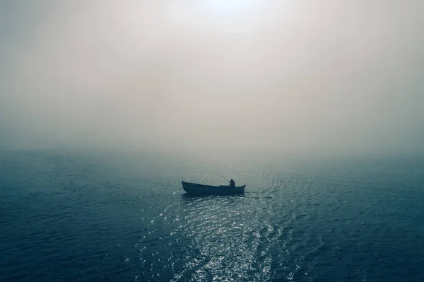Barco de pesca e pescador no mar, manhã nebulosa sobre a água — Fotografia de Stock