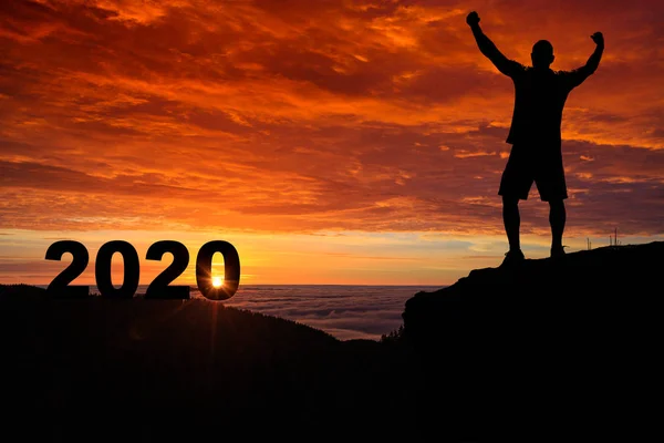 Człowiek sylwetka na szczycie góry oglądać wschód i 2020 — Zdjęcie stockowe