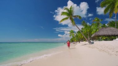 Tropik ada sahillerinde ve palmiye ağaçlarında koşan mutlu bir kadın. Punta Cana, Dominik Cumhuriyeti.