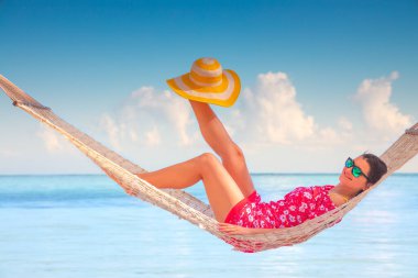 Genç bir kız hamakta dinleniyor. Uzun palmiye ağaçları altında, tropik plajda.