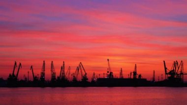 Gün batımında Varna deniz limanı, kuş siluetleri, endüstriyel vinçler ve kargo gemileri, Bulgaristan.