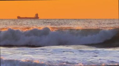 Sabahın erken saatlerinde denizde güneş doğuyor ve kargo gemisi yüzüyor.