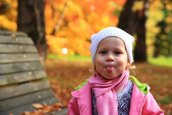 Kleines Mädchen zeigt Zunge im Herbstpark — Stockfoto