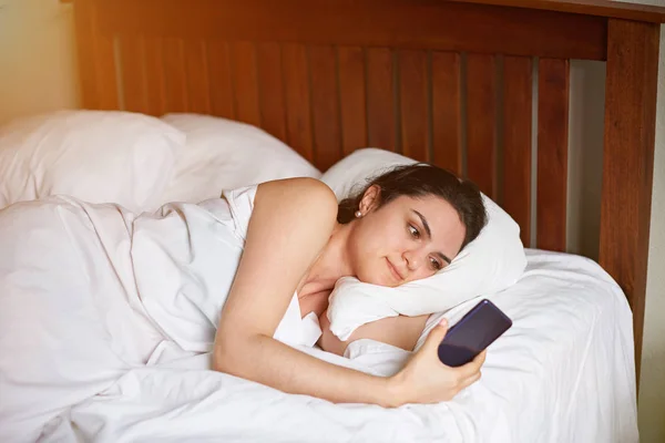 Ung kvinna i sovrum med telefon — Stockfoto