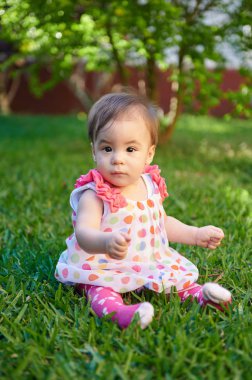 Parlak güneşli bir günde yeşil çimlerde oturan küçük kız.