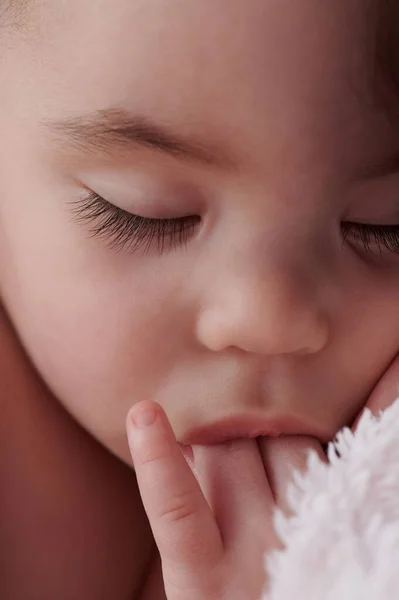 Newborn with fingers in mouth close up