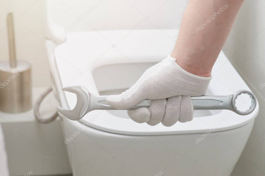 Plumber hand with wrench on toilet seat background close up view