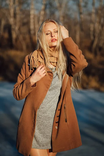 Hermosa chica en un abrigo posando sobre el fondo de una naturaleza primaveral Imagen De Stock