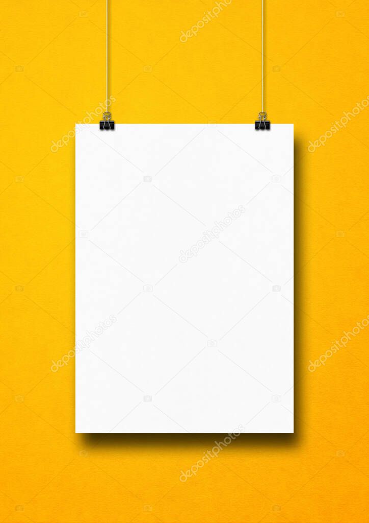 White poster hanging on a yellow wall with clips. Blank mockup template