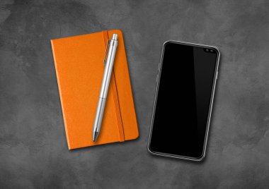 Kapalı turuncu defter, kalem ve akıllı telefon beton bir masanın üzerinde.