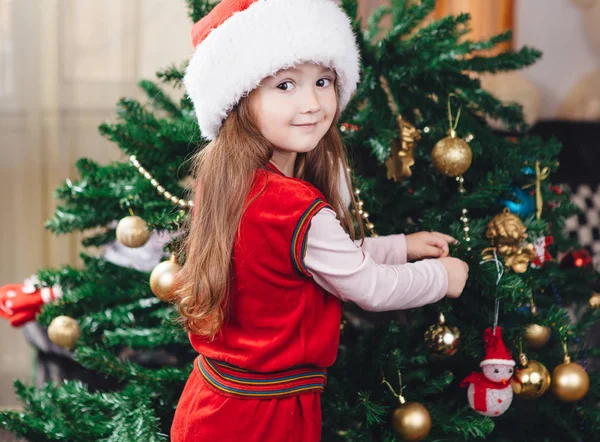 Little girl in red hat decorates a christmas tree — Stock Photo, Image