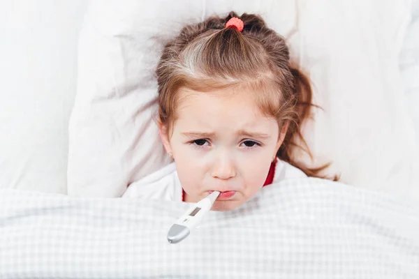 Хвора дівчина з термометром у роті лежить у ліжку — стокове фото