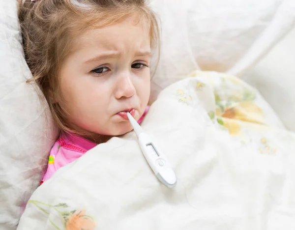 生病的小女孩抱着躺在床上的温度计 — 图库照片