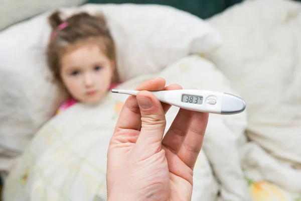 Sick little girl holding thermometer laying in bed — Stock Photo, Image