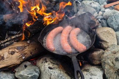 Kamp yaparken kamp ateşi üzerinde dökme demir tavada pişirme sosis. İyi ve olumlu kamp ateşi gıda.