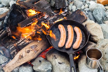 Kamp yaparken kamp ateşi üzerinde dökme demir tavada pişirme sosis. İyi ve olumlu kamp ateşi gıda.