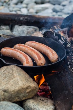 Kamp yaparken kamp ateşi üzerinde dökme demir tavada pişirme sosis. İyi ve olumlu kamp ateşi gıda.