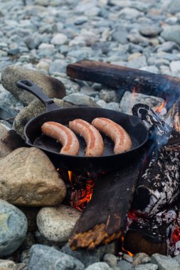 Kamp yaparken kamp ateşi üzerinde dökme demir tavada pişirme sosis. İyi ve olumlu kamp ateşi gıda.