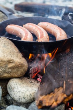 Kamp yaparken kamp ateşi üzerinde dökme demir tavada pişirme sosis. İyi ve olumlu kamp ateşi gıda.