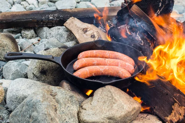 Kamp yaparken kamp ateşi üzerinde dökme demir tavada pişirme sosis. İyi ve olumlu kamp ateşi gıda.
