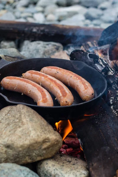 Kamp yaparken kamp ateşi üzerinde dökme demir tavada pişirme sosis. İyi ve olumlu kamp ateşi gıda.