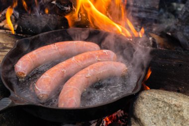 Kamp yaparken kamp ateşi üzerinde dökme demir tavada pişirme sosis. İyi ve olumlu kamp ateşi gıda.