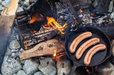 Kamp yaparken kamp ateşi üzerinde dökme demir tavada pişirme sosis. İyi ve olumlu kamp ateşi gıda.