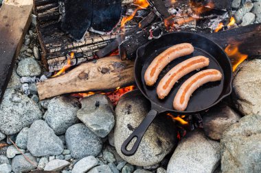 Kamp yaparken kamp ateşi üzerinde dökme demir tavada pişirme sosis. İyi ve olumlu kamp ateşi gıda.