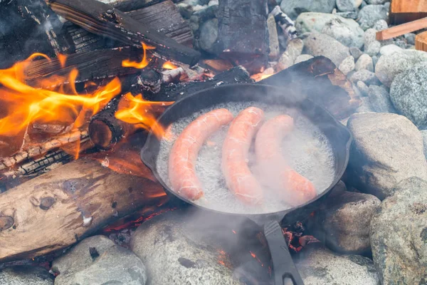 Kamp yaparken kamp ateşi üzerinde dökme demir tavada pişirme sosis. İyi ve olumlu kamp ateşi gıda.
