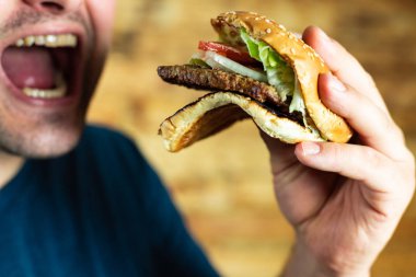 Aç genç adam agresif bir şekilde bir burger yer. Fast food