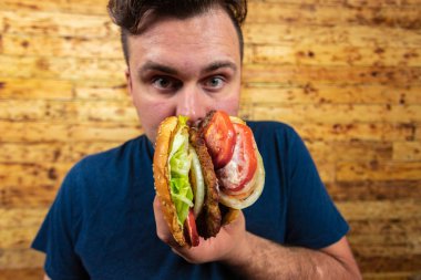 Genç yakışıklı adam lezzetli burgeriyle poz veriyor ve tadını çıkarmak üzere..