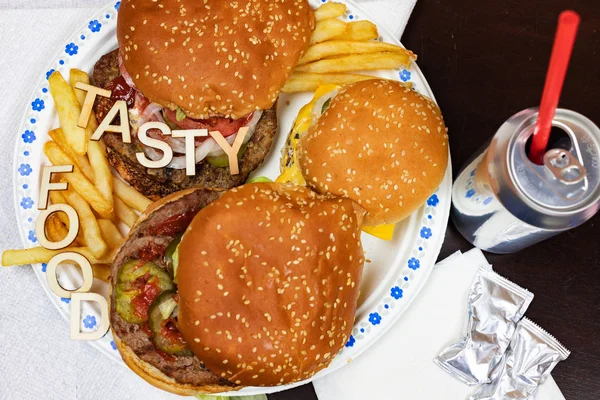Hambúrgueres suculentos e batatas fritas em um prato de papel com palavras TASTY FOOD em hambúrgueres . — Fotografia de Stock