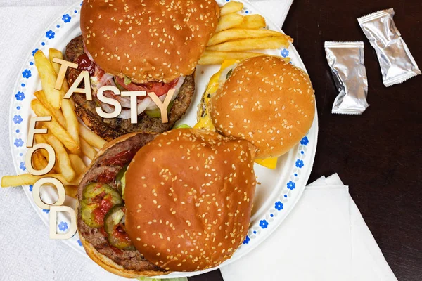Hamburguesas y papas fritas jugosas en un plato de papel con palabras TASTY FOOD en hamburguesas . —  Fotos de Stock