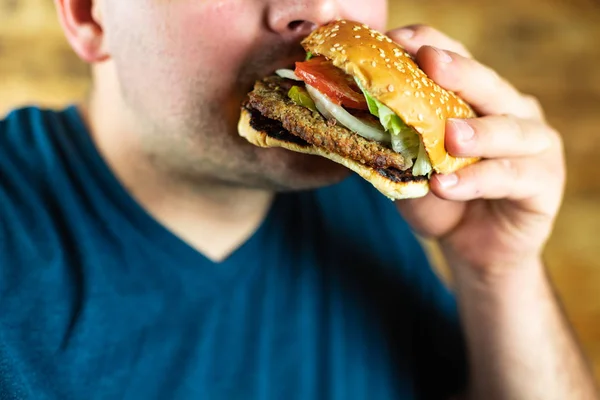 O jovem faminto come agressivamente um hambúrguer. Fast food — Fotografia de Stock