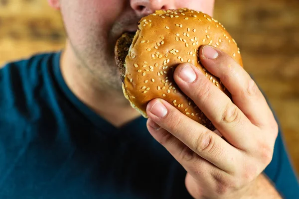 O jovem faminto come agressivamente um hambúrguer. Fast food — Fotografia de Stock