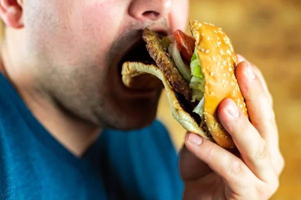 Il giovane affamato mangia aggressivamente un hamburger. Fast food — Foto Stock