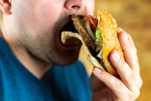 Aç genç adam agresif bir şekilde bir burger yer. Fast food