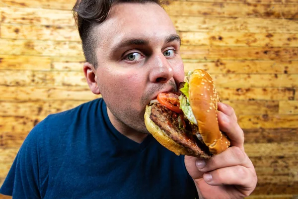Genç yakışıklı adam lezzetli burgeriyle poz veriyor ve tadını çıkarmak üzere..