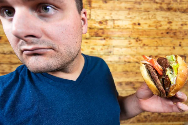 Jovem homem bonito está posando com seu saboroso hambúrguer e prestes a apreciá-lo . — Fotografia de Stock