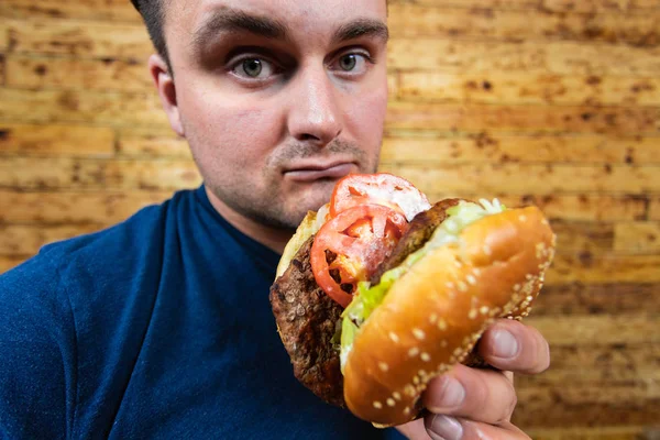 Joven hombre guapo está posando con su sabrosa hamburguesa y a punto de disfrutarlo . —  Fotos de Stock