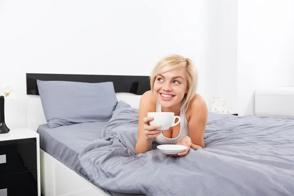 Женщина держит чашку кофе лежа на кровати — стоковое фото