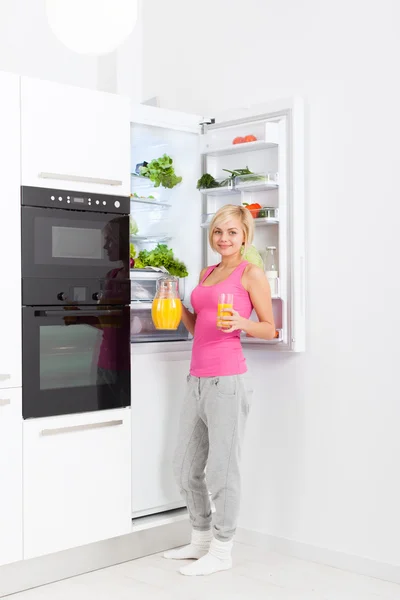 Young woman drink orange juice hold glass refrigerator — ストック写真