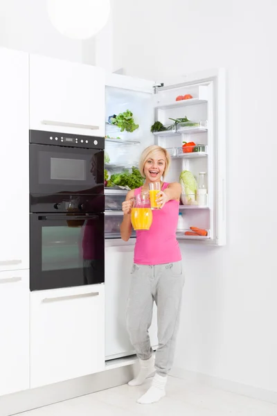 Woman drink orange juice hold glass refrigerator — Zdjęcie stockowe