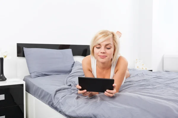 Schöne Frau liegt mit digitalem Tablet im Bett — Stockfoto