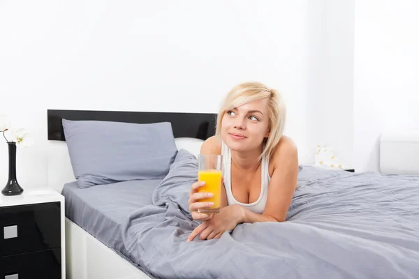 Женщина пьет апельсиновый сок, лежа на кровати — стоковое фото